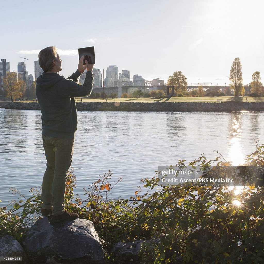 Man takes picture with digital tablet, over city