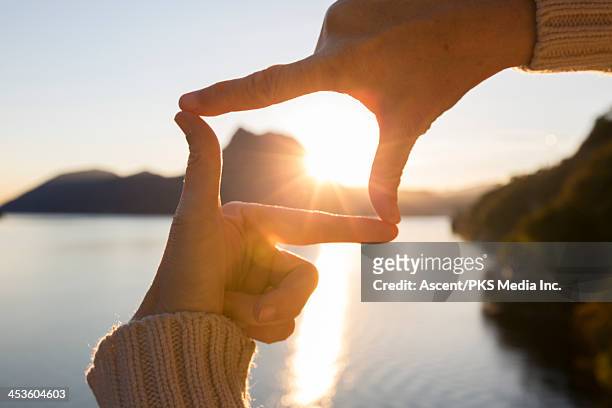 woman's hands frame sunrise over mountain lake - scherpte stockfoto's en -beelden