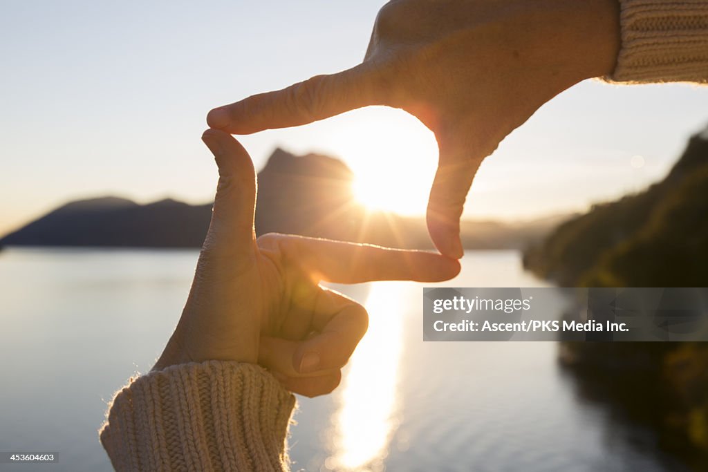 Woman's hands frame sunrise over mountain lake