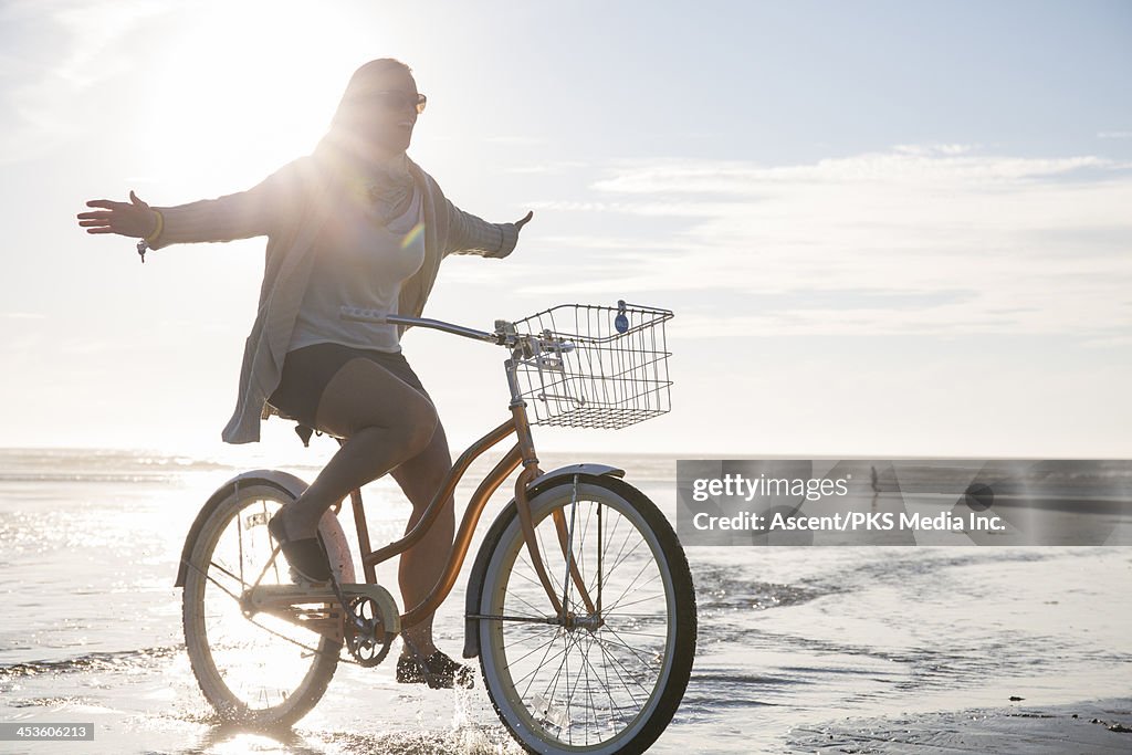 Woman rides bicycle on beach, without using hands