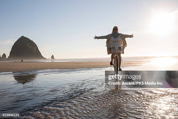 woman rides bicycle across beach, without hands - man outstretched arms stock-fotos und bilder