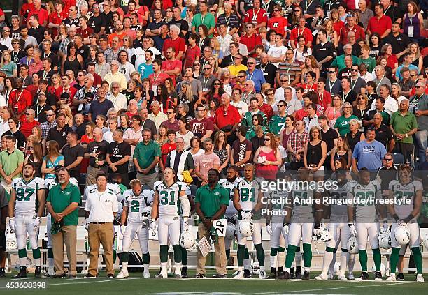 Members of the Saskatchewan Roughriders stand at attention on the sideline during the singing of the national anthem prior to playing against the...