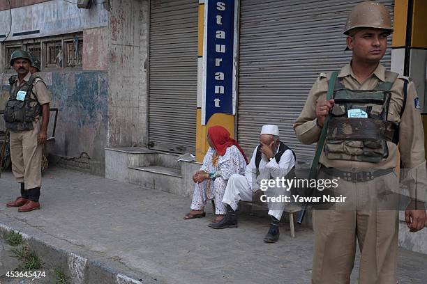 An elderly Kashmiri couple rests on the steps of shuttered shop as Indian government forces stand guard during India's Independence Day celebrations...