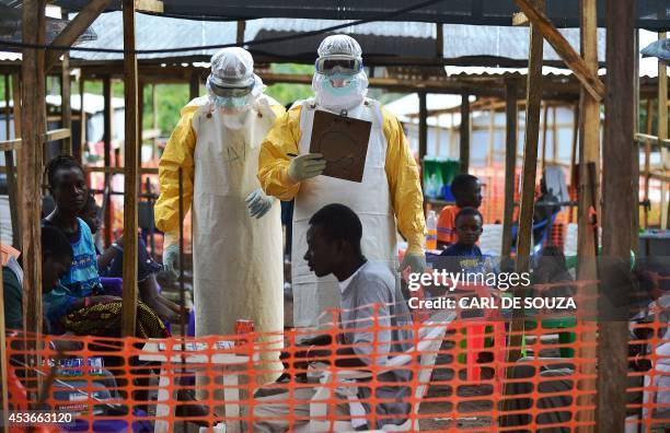 An MSF medical worker, wearing protective clothing relays patient details and updates behind a barrier to a colleague at an MSF facility in Kailahun,...