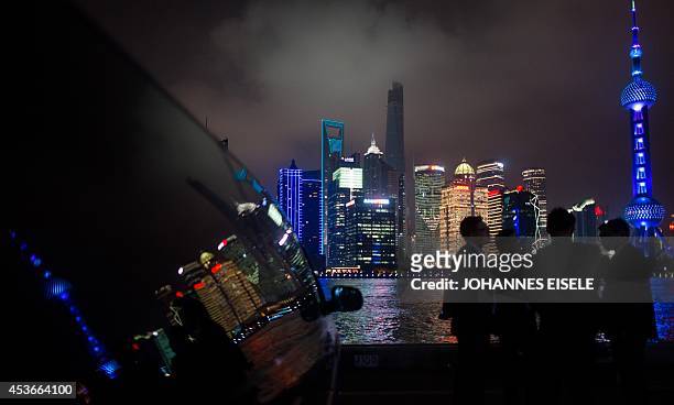 This photo taken on August 15, 2014 shows people standing next to luxury cars as they wait for their owners in front of the skyline of the Lujiazui...