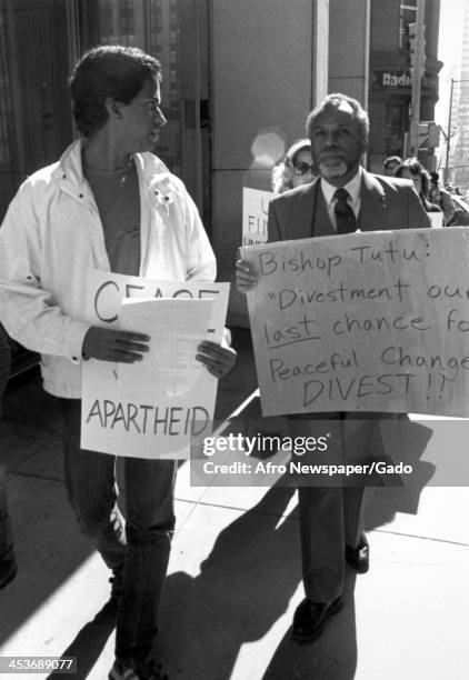 Protestors march holding signs quoting Bishop Tutu in support of ending South African apartheid, 1980.