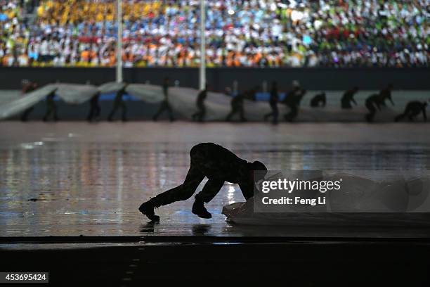 Soldiers remove water from the pitch in the rain before the opening ceremony for the Nanjing 2014 Summer Youth Olympic Games at the Nanjing Olympic...