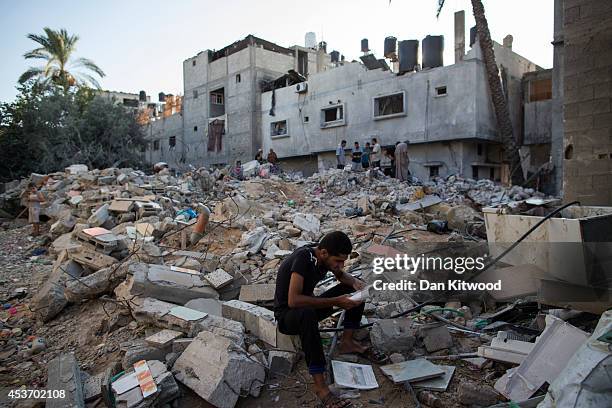 Palestinian man reads items found in the rubble of a destroyed area of housing on August 16, 2014 in Gaza City, Gaza. A five-day ceasefire between...