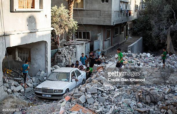 Group of Palestinian men push a car that had become trapped by rubble out of an area of destroyed housing on August 16, 2014 in Gaza City, Gaza. A...