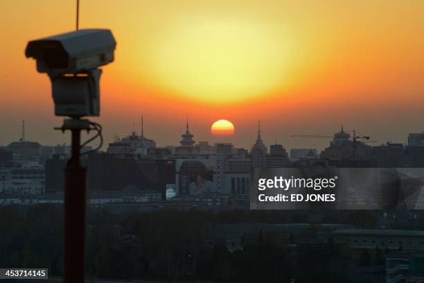 The sun sets behind the Beijing skyline and a security camera, on December 5, 2013. Beijing is the second most expensive city in Asia for...