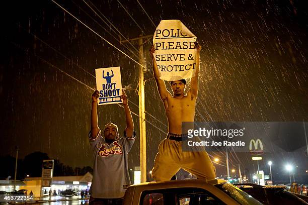 Demonstrators protesting the shooting death of Michael Brown hold signs on August 16, 2014 in Ferguson, Missouri. Violent outbreaks have taken place...