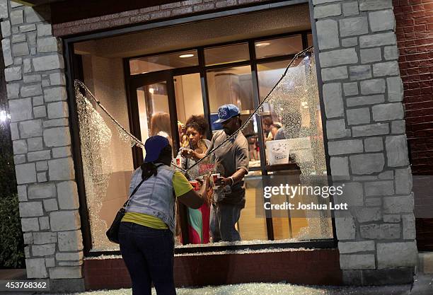 People stand near a broken window which was damaged as demonstrators were protesting the shooting death of teenager Michael Brown by police August...