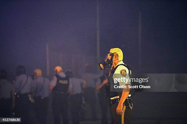 Police in protective clothing advance through a cloud of tear gas toward demonstrators protesting the killing of teenager Michael Brown on August 17,...