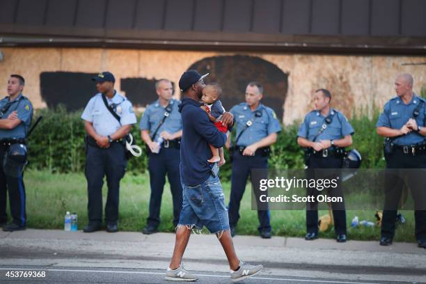 Man carries his child past a row of police tasked with keeping the peace as demonstration to protest the killing of teenager Michael Brown on August...