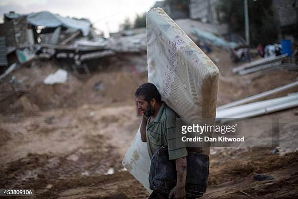 Man walks through the ruins of demolished homes with a mattrass on August 15, 2014 in Khuza'a, Gaza. A new five-day ceasefire between Palestinian...