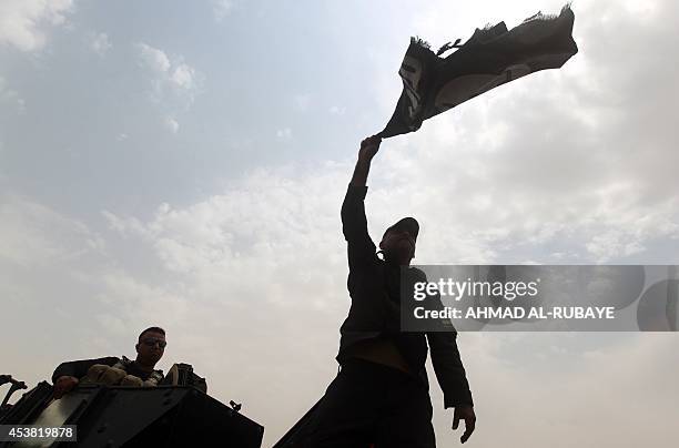 Members of the Iraqi anti-terrorism forces wave a trademark Islamists flag after securing a checkpoint from Sunni militants in the village of...