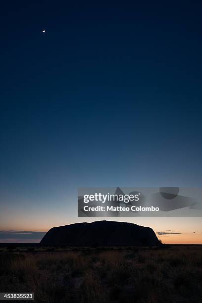 Night with small moon over Uluru, just before sunrise, in the red sand desert landscape of Northern Territory, Australia. Uluru, also known as Ayers...