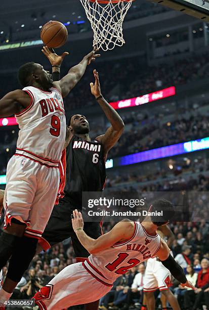 LeBron James of the Miami Heat goes up for a shot over Kirk Hinrich and Loul Deng of the Chicago Bulls at the United Center on December 5, 2013 in...