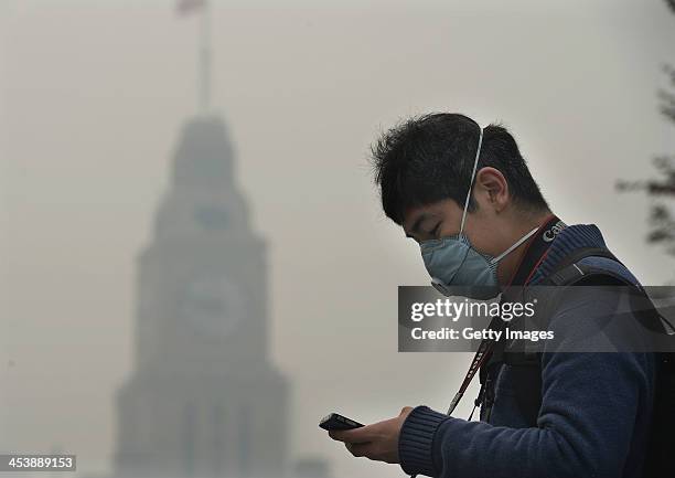 Man wearing mask checks his mobile phone at The Bund on December 6, 2013 in Shanghai, China. Heavy smog continued to hit northern and eastern parts...