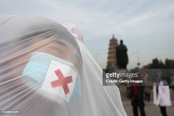College students wearing masks pose with a plastic bag during a performance art to raise awareness of air pollution on December 5, 2013 in Xi an,...
