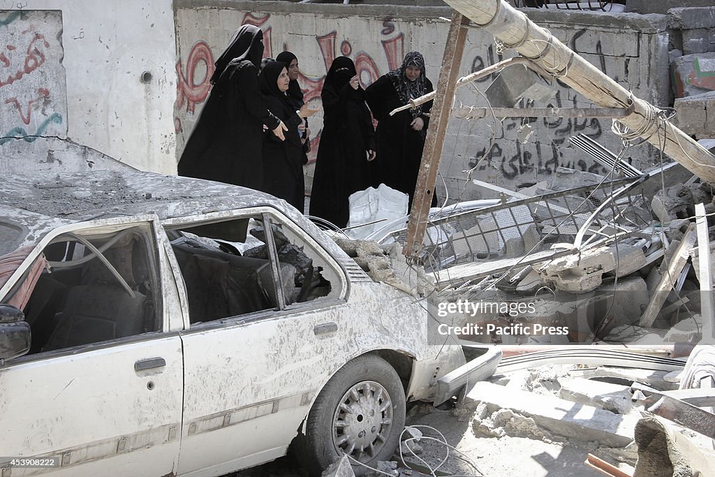 Palestinian women walk past a destroyed vehicle, which...