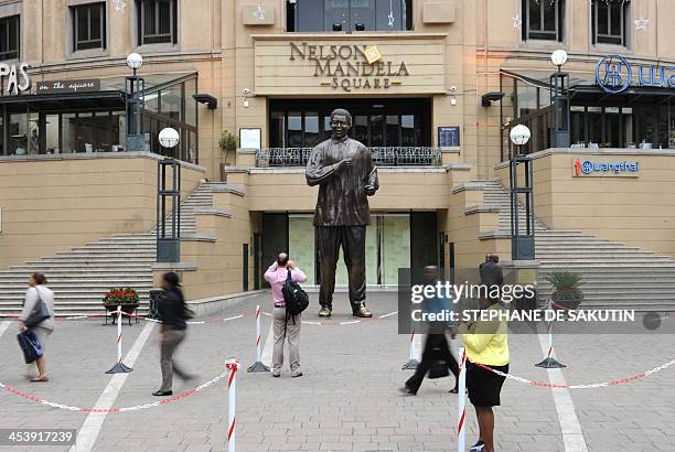 People walk on December 6, 2013 in front of a statue of late South African President Nelson Mandela in Johannesburg, as many people are expected to...