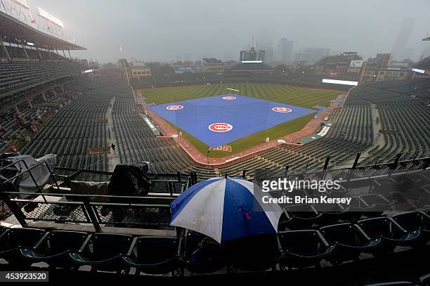 Fan huddles under an umbrella as rain falls, delaying the restart of a suspended game from August 19 between the Chicago Cubs and the San Francisco...