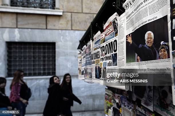 People pass newspapers featuring headlines about South African former President Nelson Mandela, in Athens on December 6, 2013. Mandela, the revered...