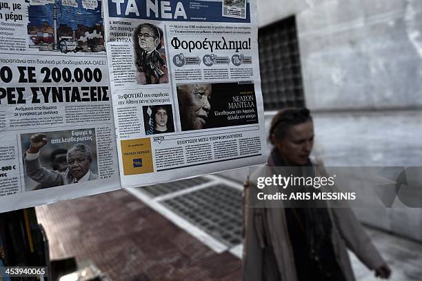 Woman passes newspapers featuring headlines about South African former President Nelson Mandela, in Athens on December 6, 2013. Mandela, the revered...