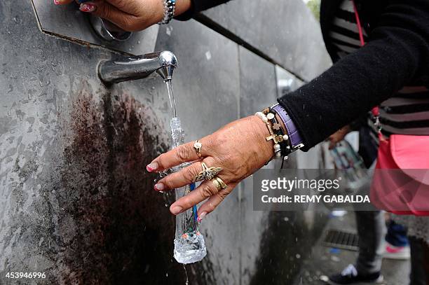 Gypsy woman fills a "Our Lady of Lourdes " moulded bottle with Lourdes water prior to the start of the annual Marian procession on August 21, 2014 as...