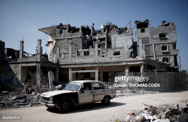 Palestinian man drives his old Peugeot 504 car past destroyed buildings in the northern Gaza Strip city of Beit Hanun on August 22, 2014. The Hamas...