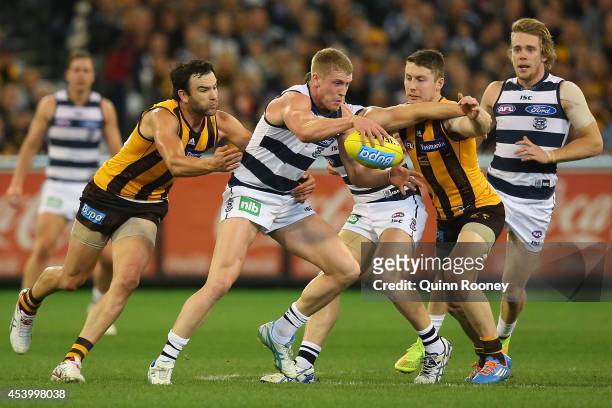 Josh Caddy of the Cats kicks whilst being tackled by Jordan Lewis and Liam Shiels of the Hawks during the round 22 AFL match between the Hawthorn...