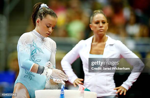 Jazmyn Foberg applies chalk to her hands before competing on the uneven bars as her coach, Maggie Haney, looks on in the junior women finals during...