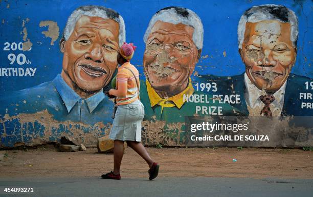 Residents walks past murals of late South African former president Nelson Mandela in Soweto, near Johannesburg, on December 7 two days after his...