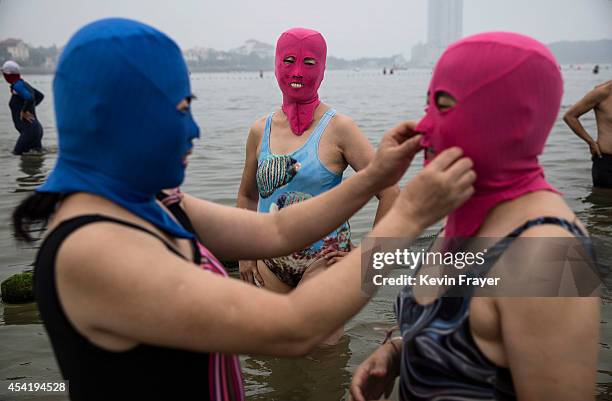 Chinese woman adjusts another's face-kini as they swim on August 21, 2014 in the Yellow Sea in Qingdao, China. The locally designed mask is worn by...