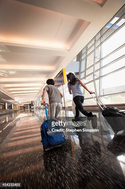 siblings rush through airport w/carry-on luggage - luggage trolley stock-fotos und bilder