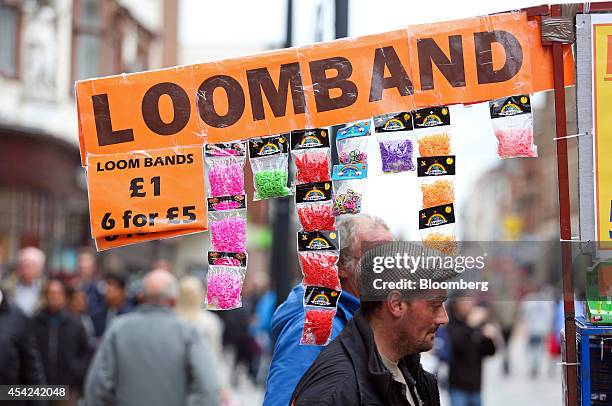 Loom Band" sign hangs above bags of colored rubber bands, used to make Rainbow Loom band jewelry, at a market stall in Derby, U.K., on Tuesday, Aug....