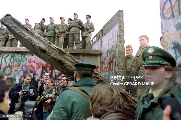 Two West German policemen prevent people from approaching as East German Vopos stand on and near a fallen portion of the Berlin Wall 11 November...