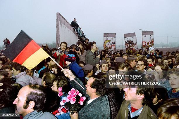 An East Berliner with West german flag and flowers enters West berlin amidst a crowd of East germans flooding through the recently made opening in...