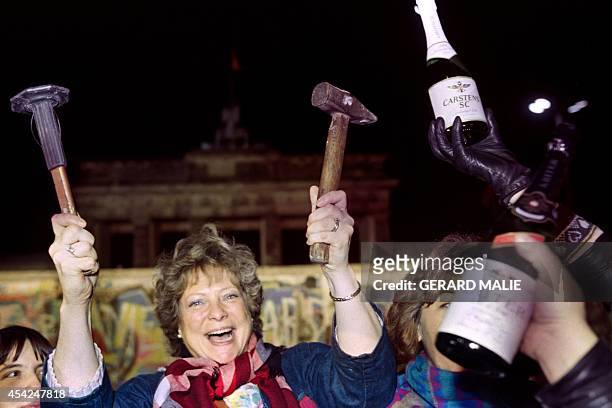 Berliner holds up a hammer and a chisel early on November 15, 1989 in front of the wall at the Brandebourg Gate partly visible behind it as a crowd...