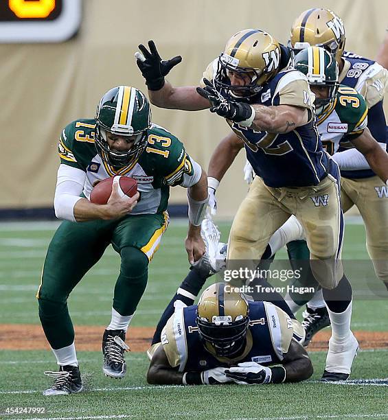 Quarterback Mike Reilly of the Edmonton Eskimos gets away from Louie Richardson and Ejiro Kuale of the Winnipeg Blue Bombers during a CFL football...