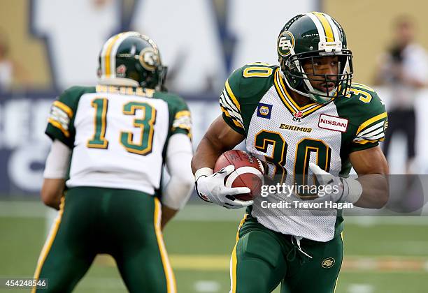 John White of the Edmonton Eskimos carries a handoff from quarterback Mike Reilly during a CFL football game against the Winnipeg Blue Bombers at...