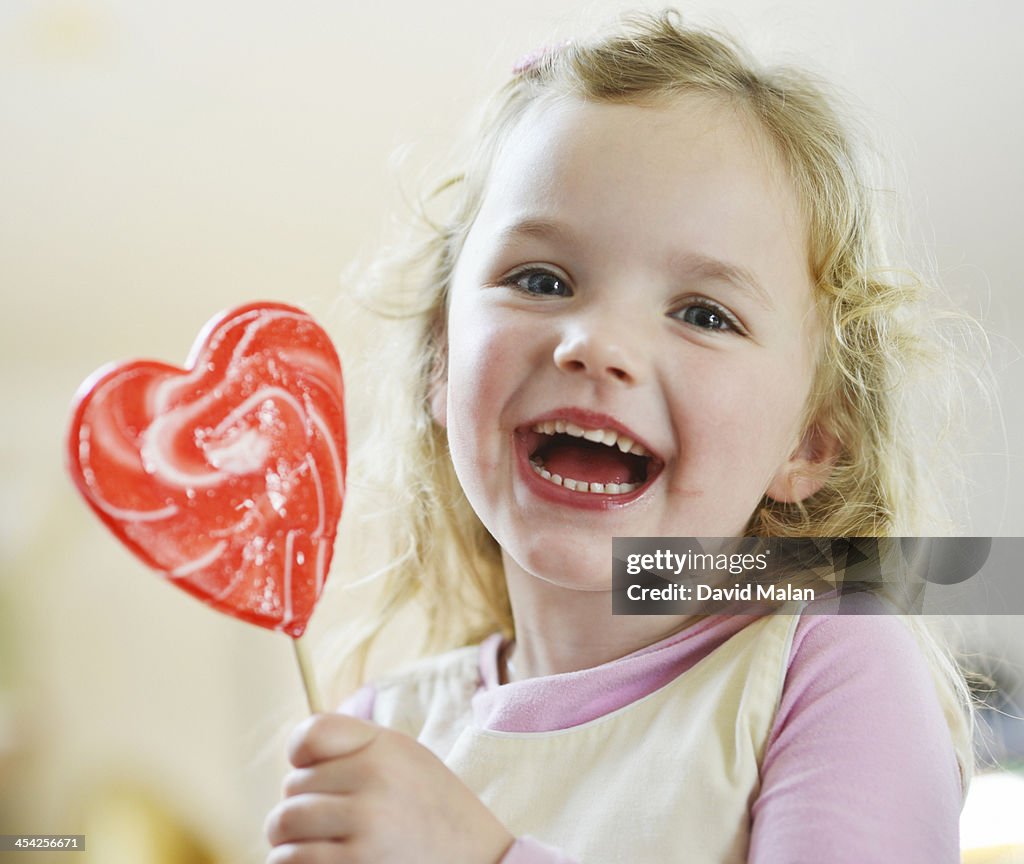 Girl laughing holding a heart shaped lollipop