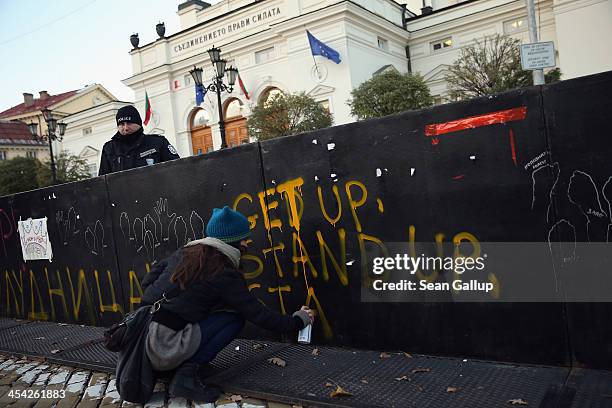 An activist protesting against government and police corruption spray paints a barrier in front of the Bulgarian Parliament Building as a policeman...