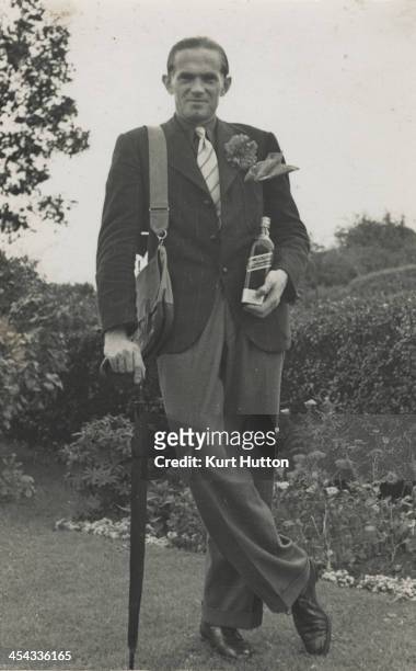 German-born photographer Kurt Hutton leaning on an umbrella and holding a bottle of whisky in the garden of his home in Hampstead Garden Suburb,...