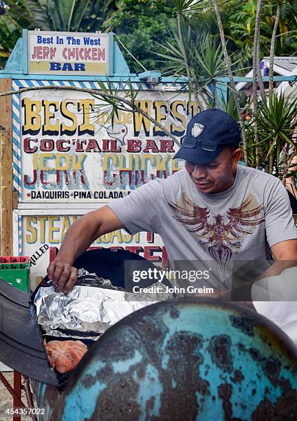 Jamaican man prepares jerk chicken in an oil barrel grill.