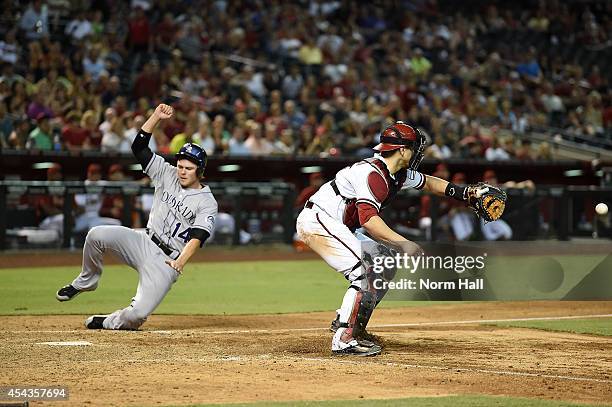 Josh Rutledge of the Colorado Rockies scores on a sacrific fly during the eighth inning as Miguel Montero of the Arizona Diamondbacks waits for the...