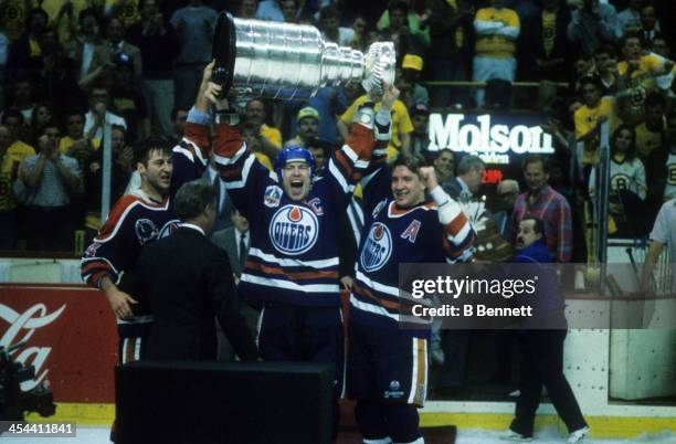 Mark Messier of the Edmonton Oilers hoists the Stanley Cup over his head and shouts as he and teammates Kevin Lowe and Jari Kurri celebrate after...