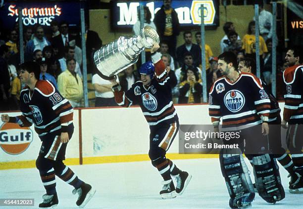 Mark Messier of the Edmonton Oilers hoists the Stanley Cup Trophy over his head as his teammates Craig Simpson and goalie Bill Ranford celebrate...