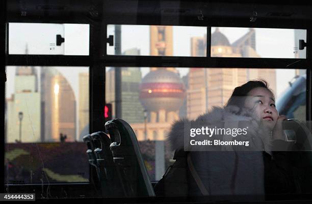 Bloomberg's Best Photos 2013: A woman looks out from a bus window as it moves along the Bund while buildings stand in the Lujiazui district in...